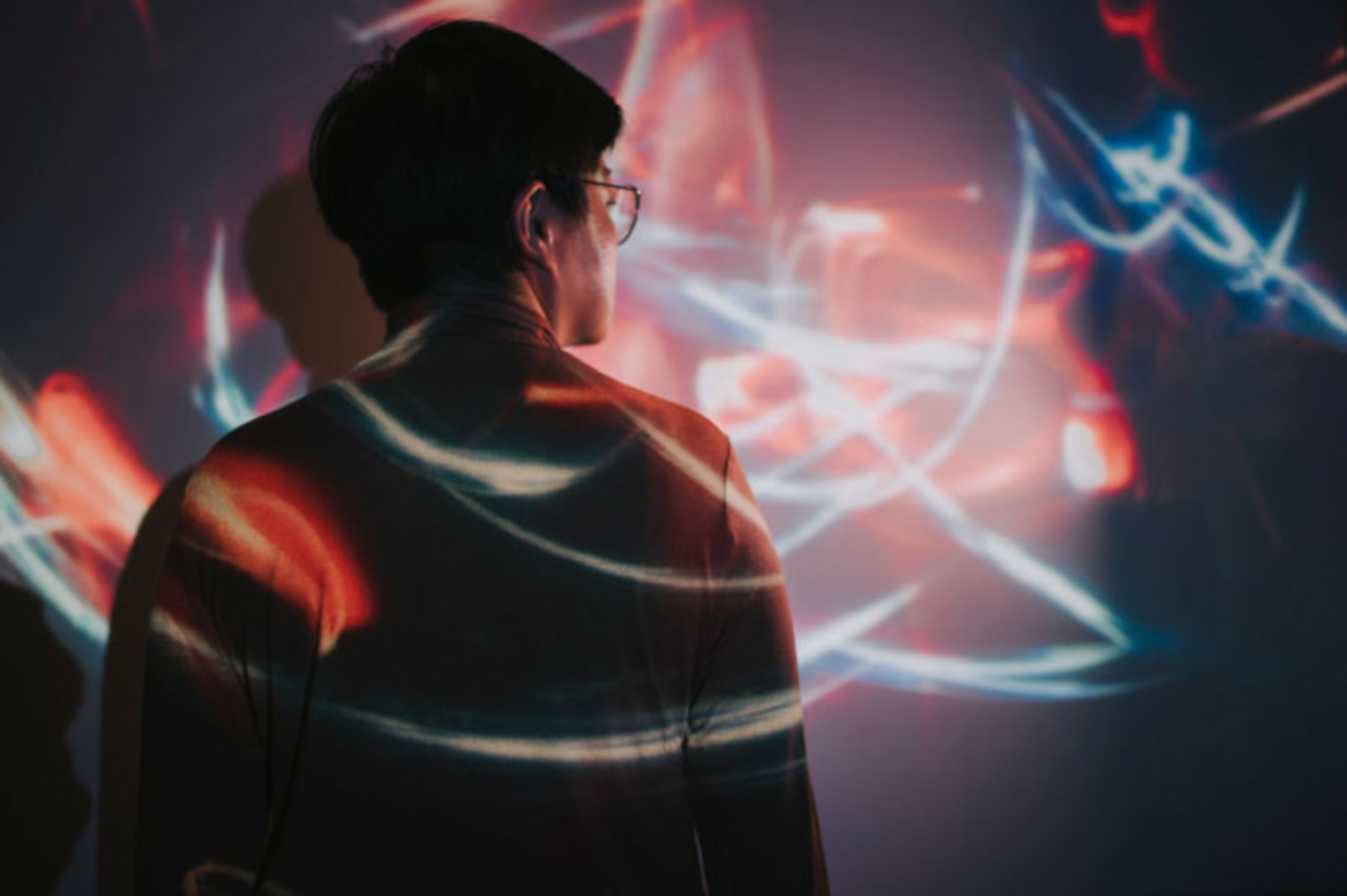 Person steht vor einer Wand und wird von Lichtern angestrahlt, gestelltes Bild.